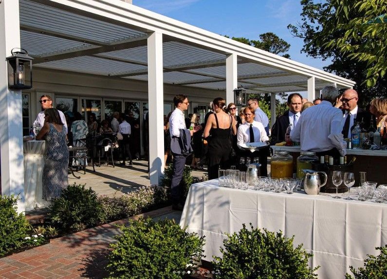 Outdoor buffet at a sunny patio reception with guests mingling under a white pergola.