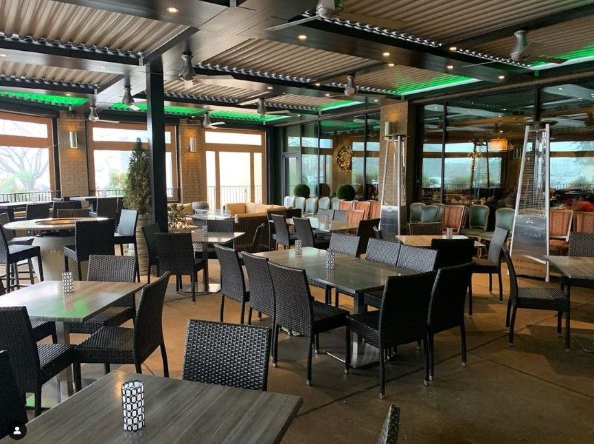 Empty outdoor restaurant patio with tables, chairs, and large windows under a covered roof