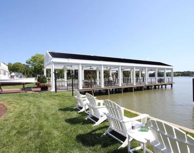 White dockside pavilion with chairs on a grassy shore beside calm water under a clear sky