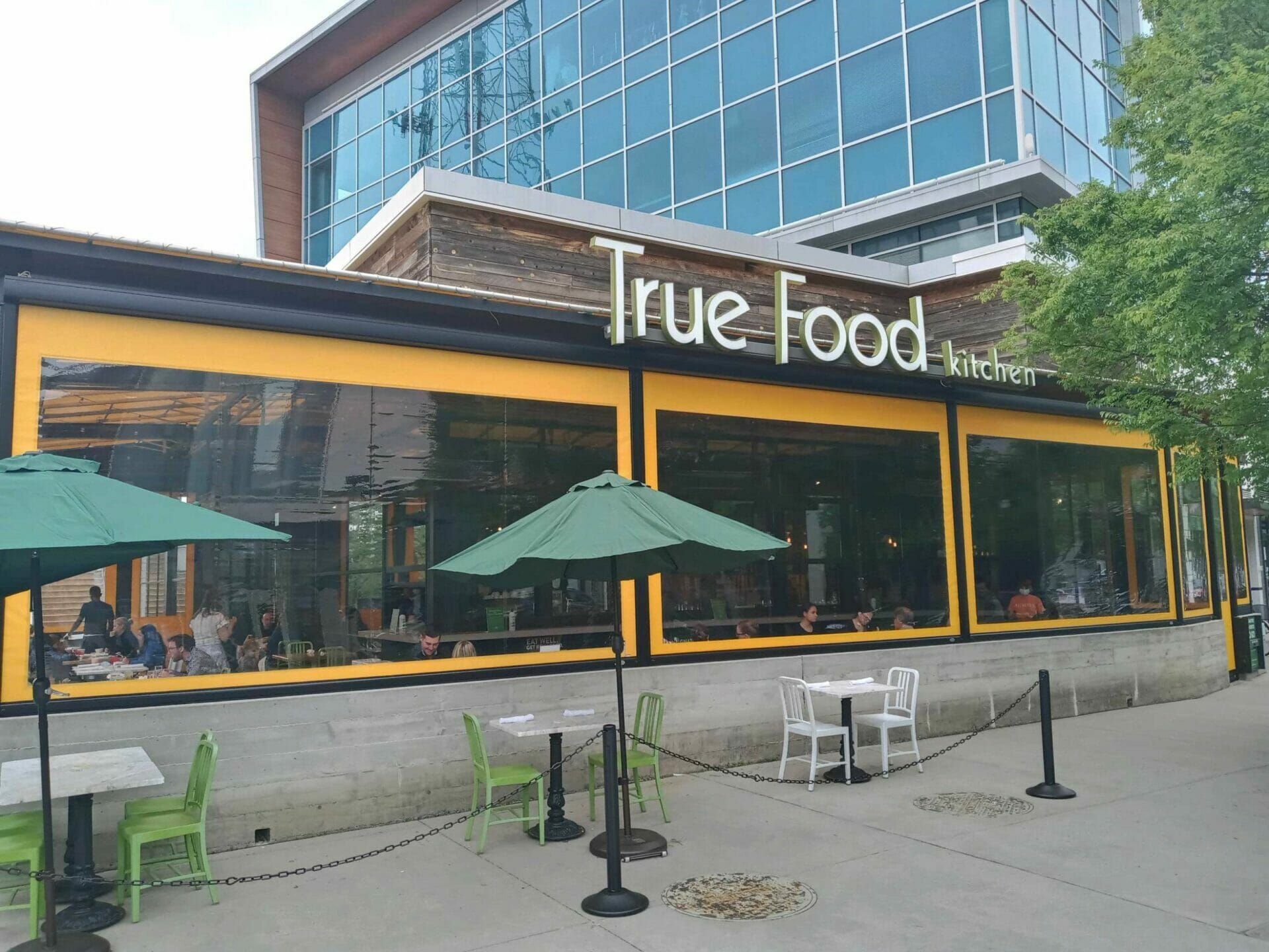 Exterior of True Food restaurant with green umbrellas and outdoor seating on a sunny day