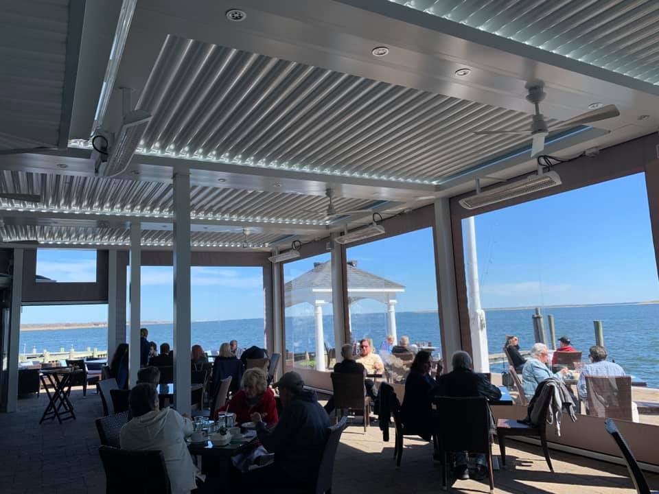 People seated at a seaside restaurant under a covered patio, overlooking the ocean