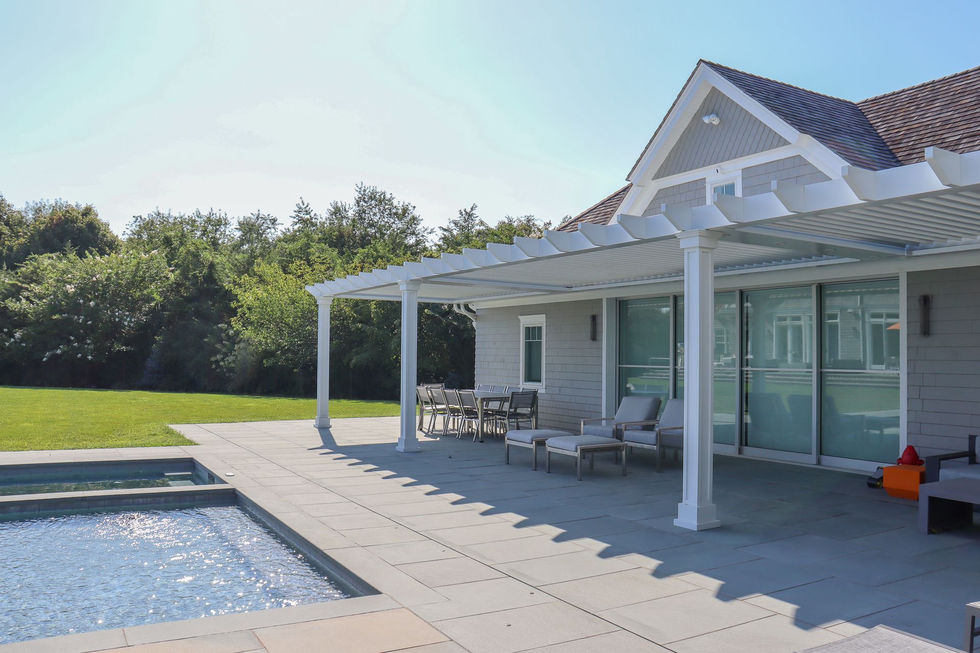 Back patio with a pool, white columns, and outdoor seating beside a modern house