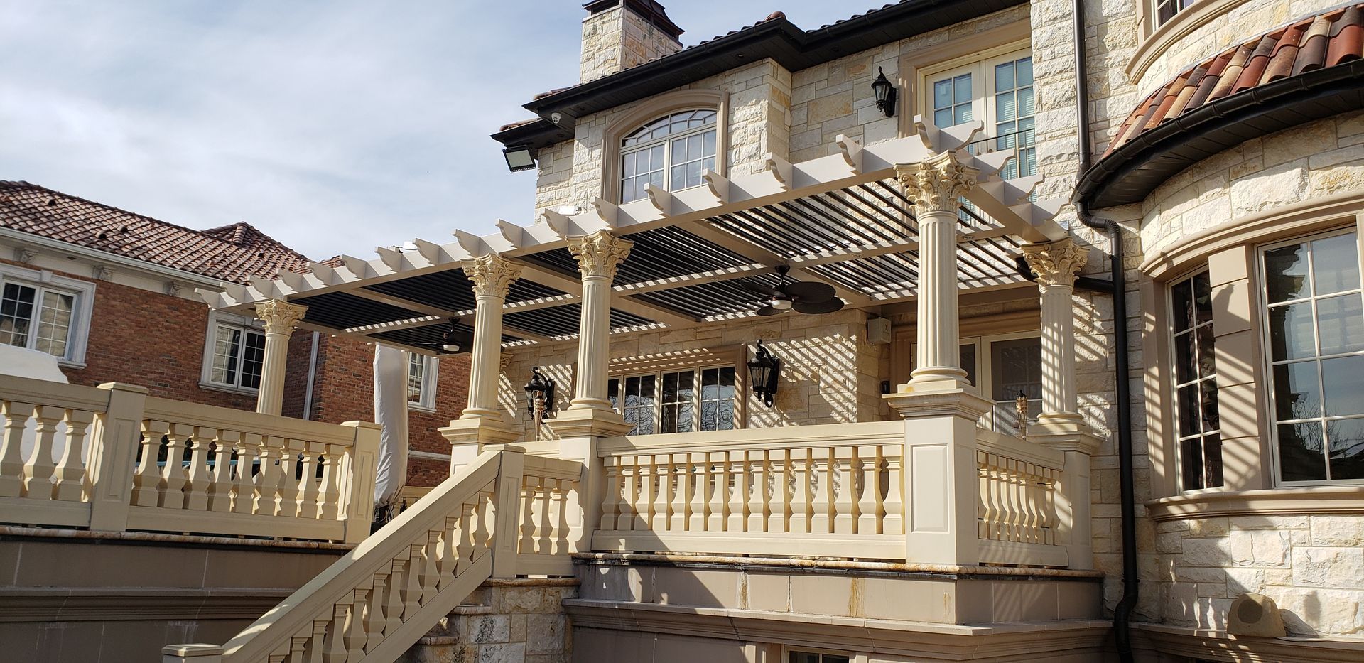 Stone patio with cream pergola and staircase in front of a beige house