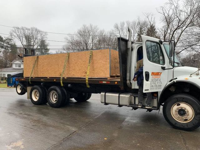 A white flatbed truck carrying a large wooden crate is parked on a paved street during an overcast day.