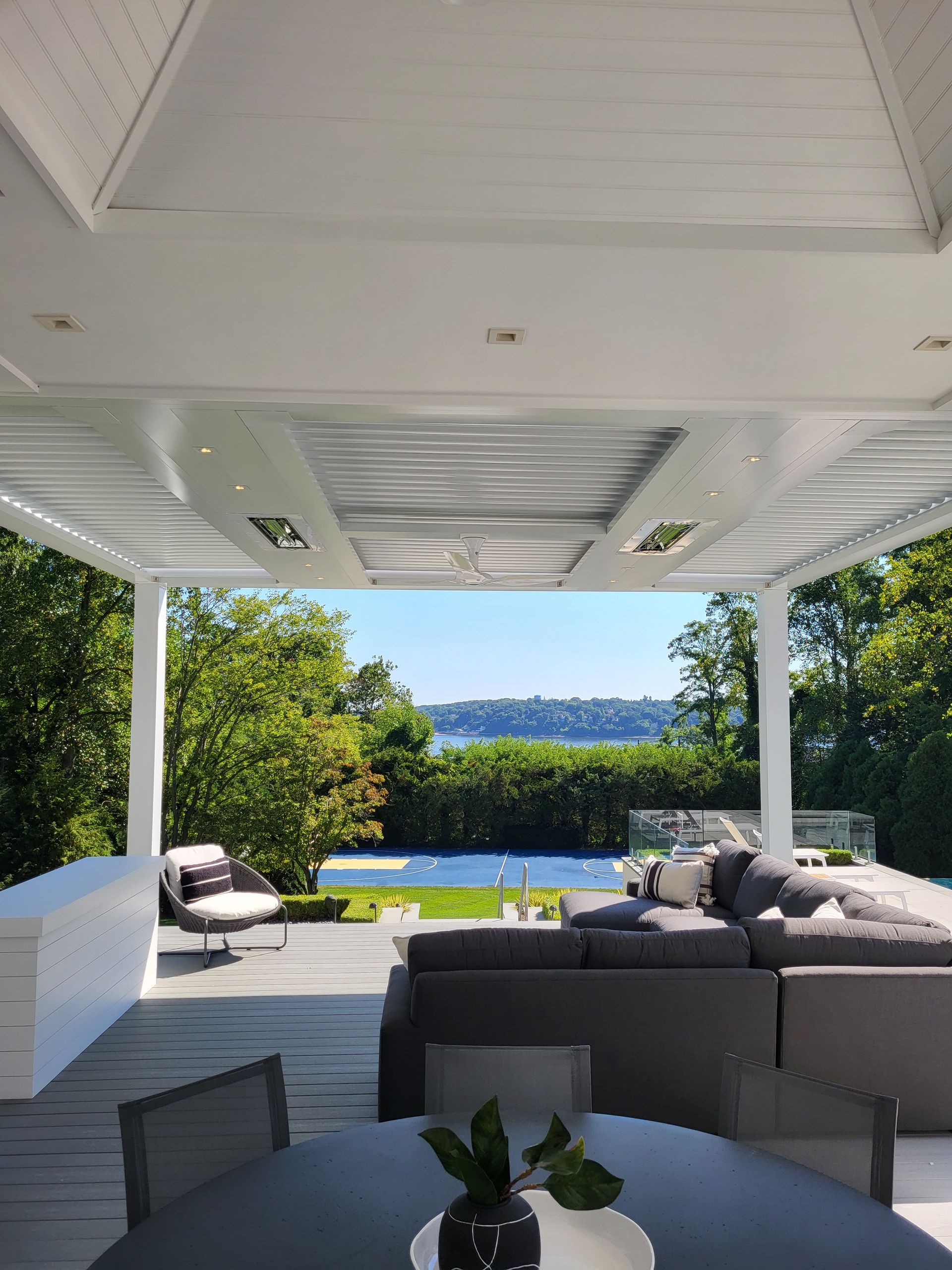 Covered patio lounge with gray seating, pool, and a view of greenery and distant city skyline
