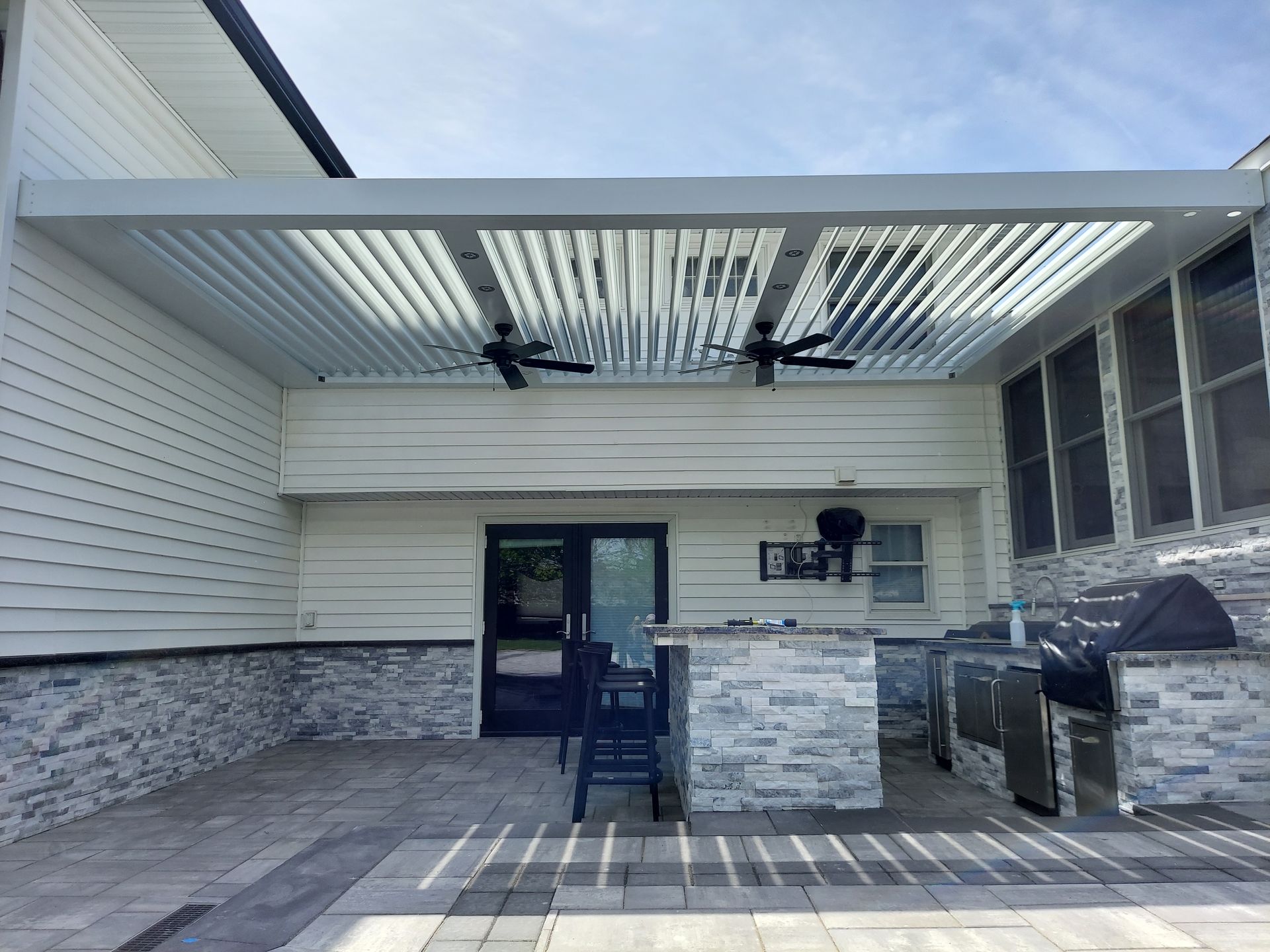 Covered patio with ceiling fans, stone columns, and a glass door entrance