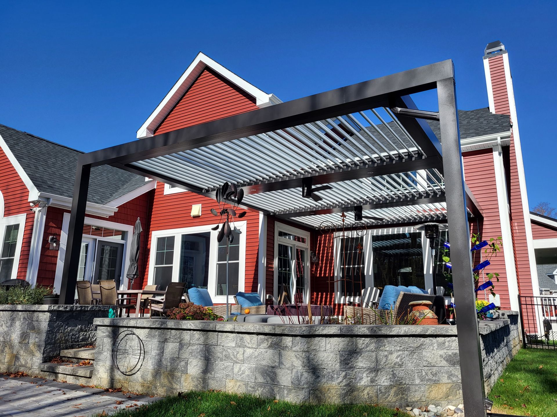 Red house patio with a black pergola and outdoor seating behind a low stone wall