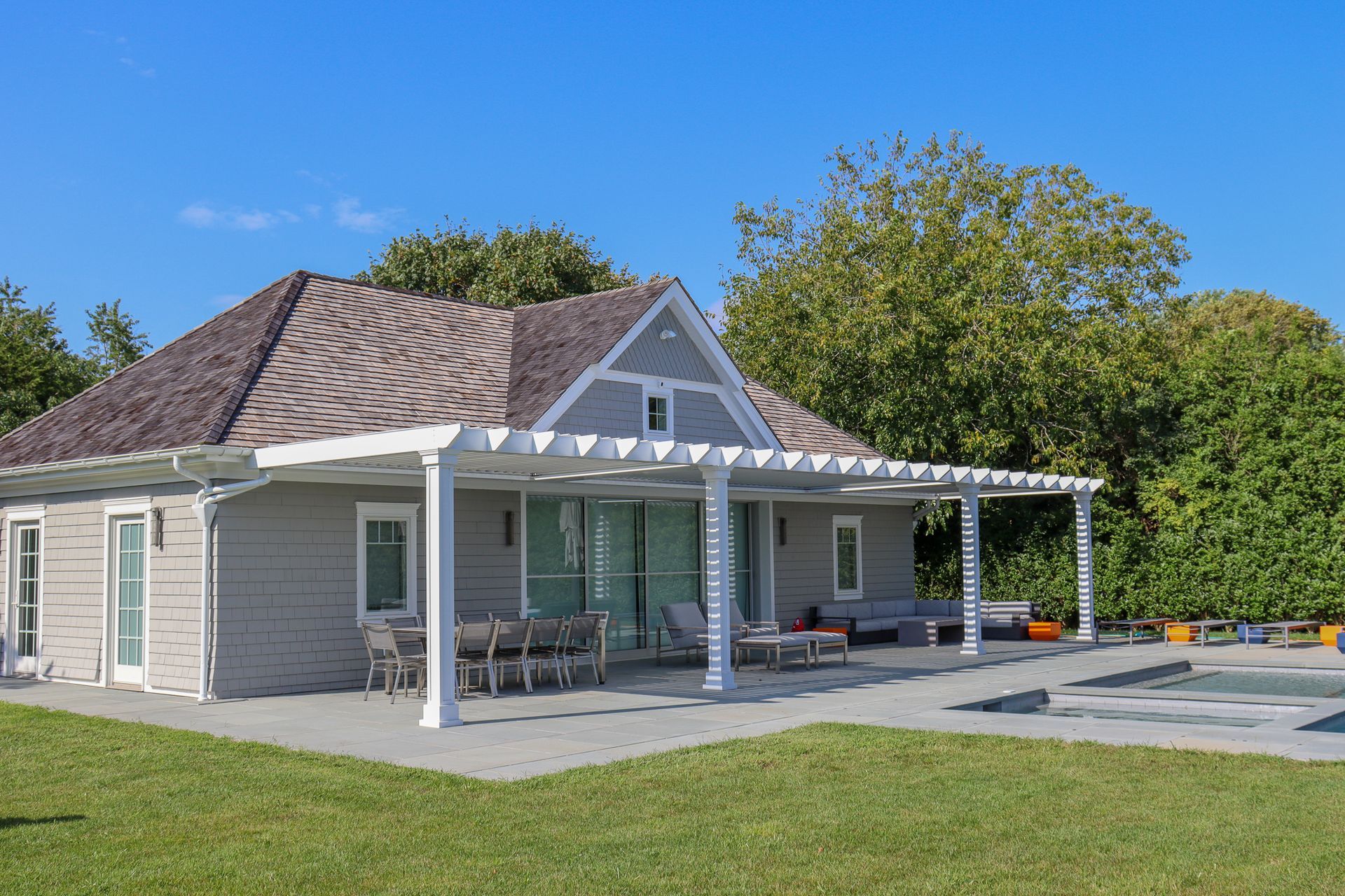 Small white house with a covered porch, dark shingled roof, and lawn under a clear blue sky