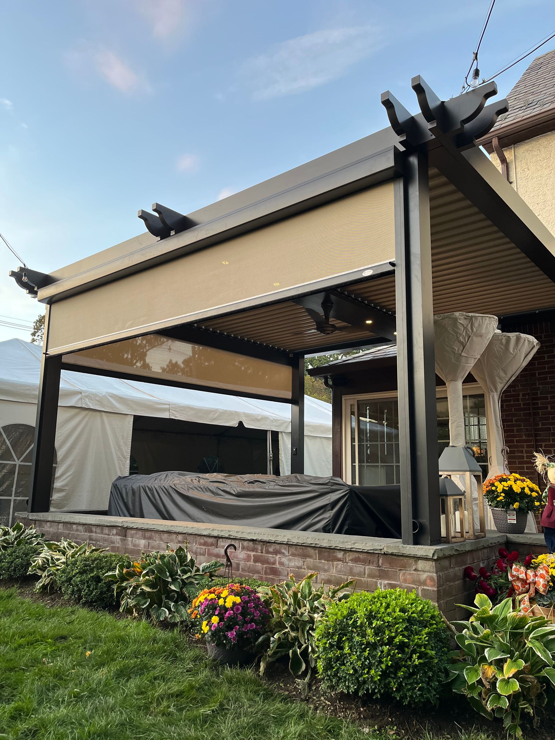 Patio with beige retractable awning, stone wall, and colorful flower beds in a garden courtyard.