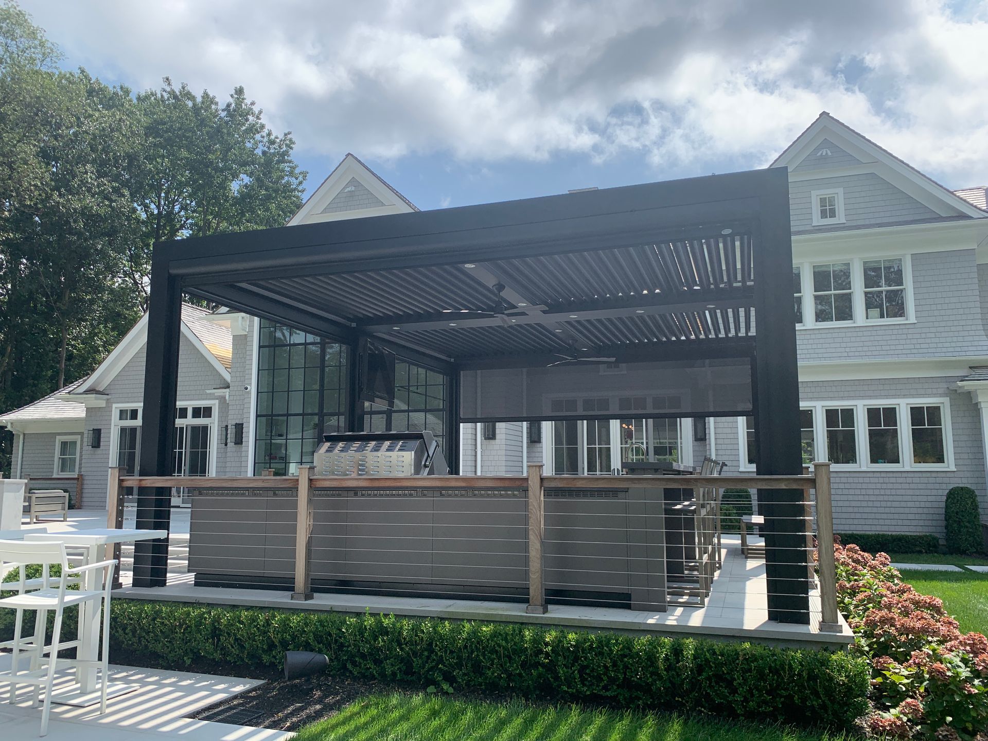 Covered outdoor bar on a house patio with black pergola and wood slat counter under a sunny sky