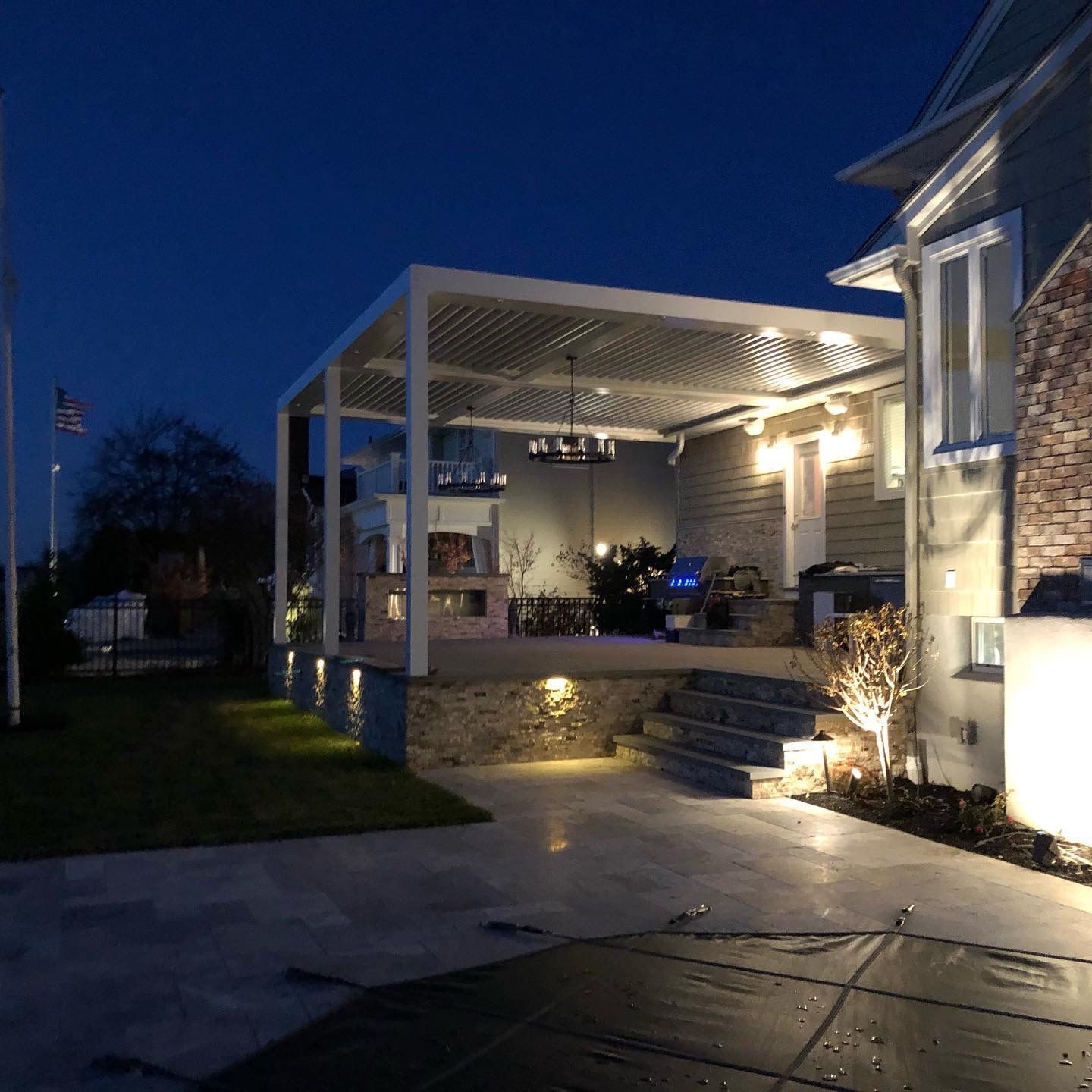Nighttime patio with a covered outdoor seating area, steps, and warm lights beside a house.