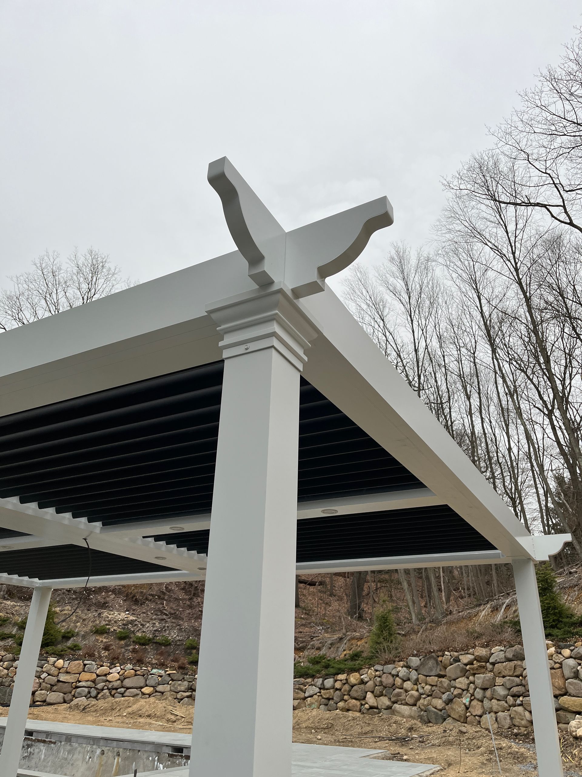 White bird sculpture atop a pavilion roof with white columns and black slats against a cloudy sky.