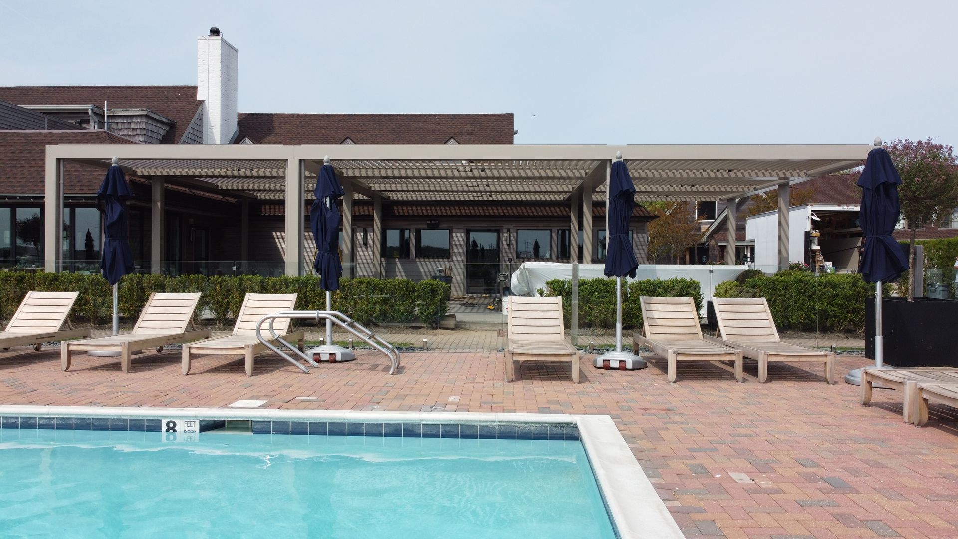 Poolside lounge chairs beside a turquoise swimming pool and covered patio with pergola.