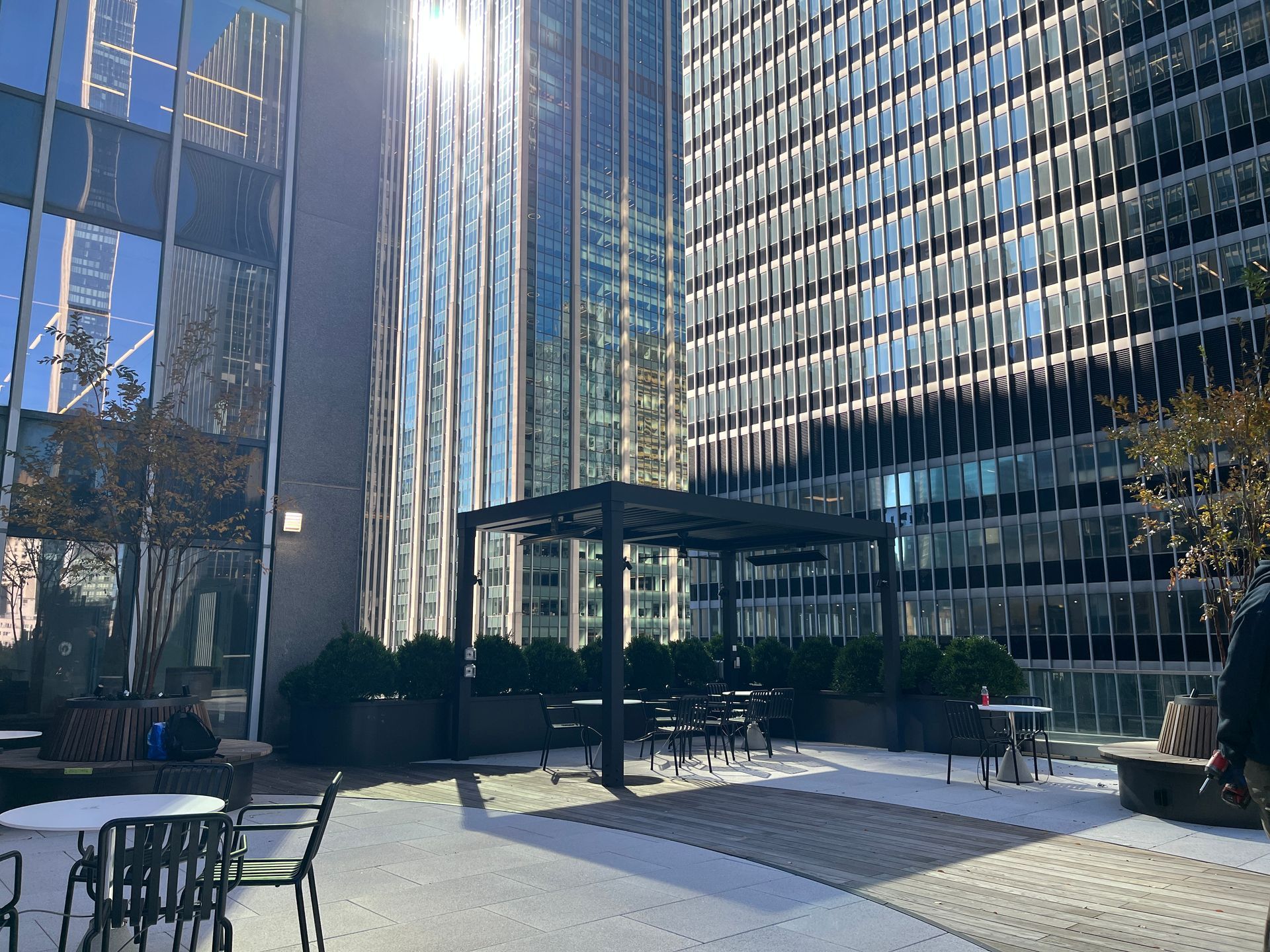 Modern office plaza with glass skyscrapers, outdoor seating, and a central courtyard under bright sunlight