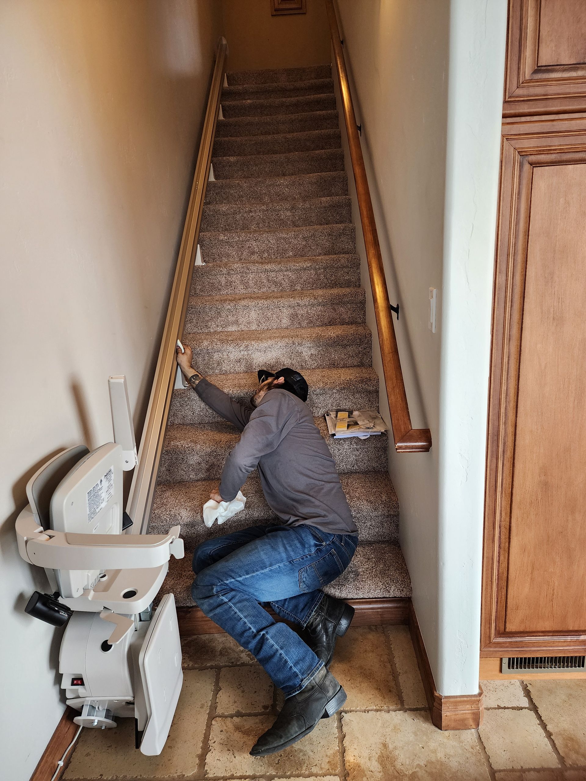 a man is kneeling down next to a stair lift in a hallway.