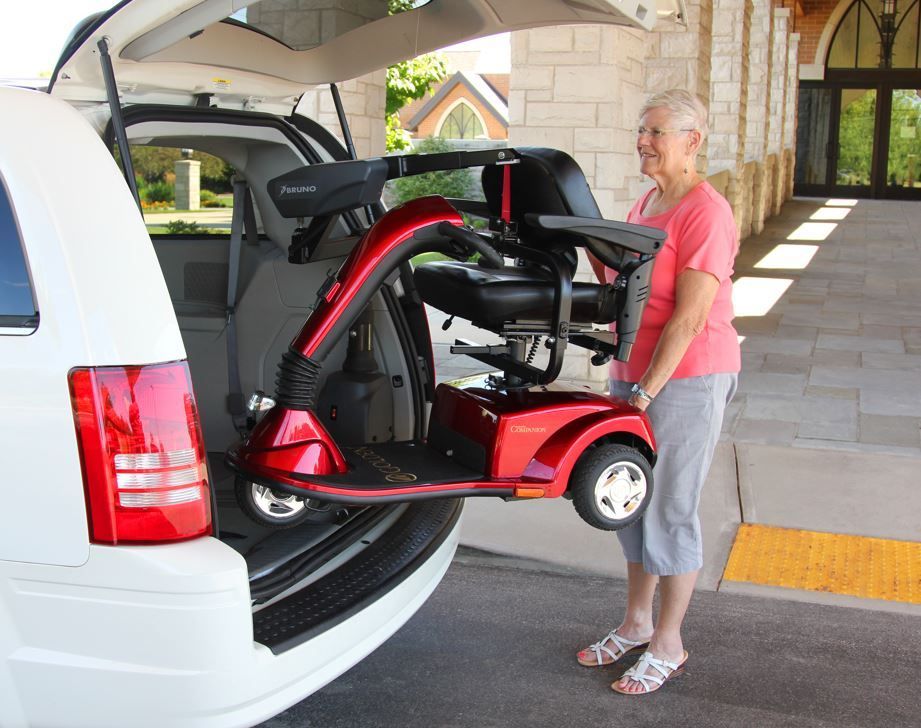 A woman is loading a red mobility scooter into the back of a white van