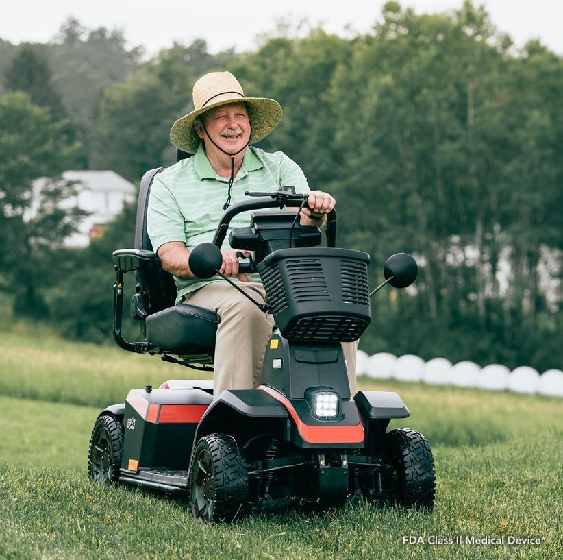 An elderly man is riding a mobility scooter in a grassy field.