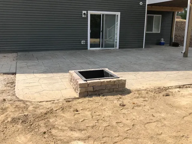 A fire pit is sitting on the side of a patio next to a house.