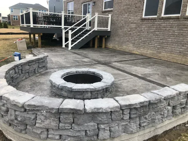 A fire pit is surrounded by a stone wall on a patio.