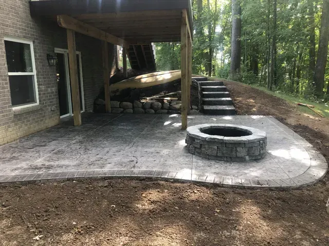 A patio with a fire pit and stairs under a deck.