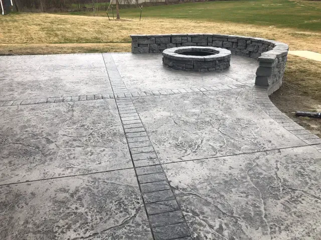 A concrete patio with a fire pit and a stone wall.