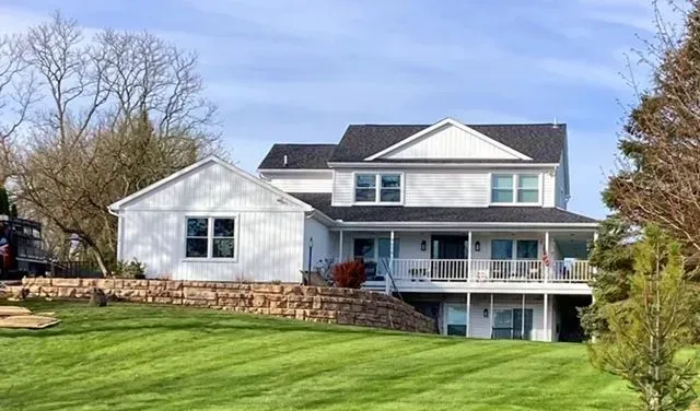 A large white house with a black roof is sitting on top of a lush green hill.