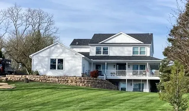 A large white house with a black roof is sitting on top of a lush green hill.