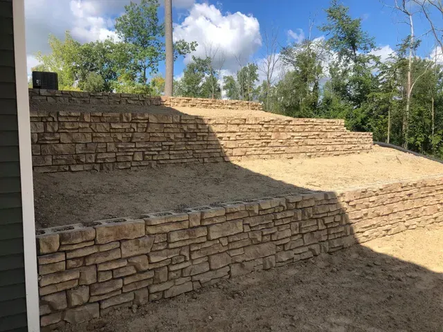 A retaining wall sits on top of a hill next to a house.