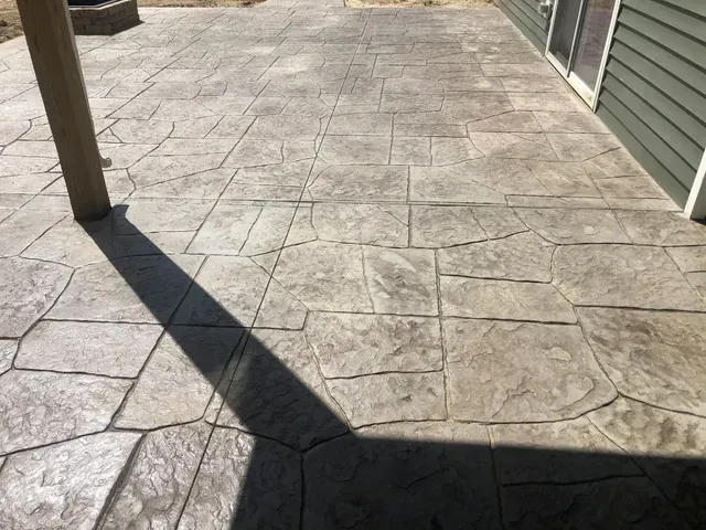 A concrete patio with a green house in the background