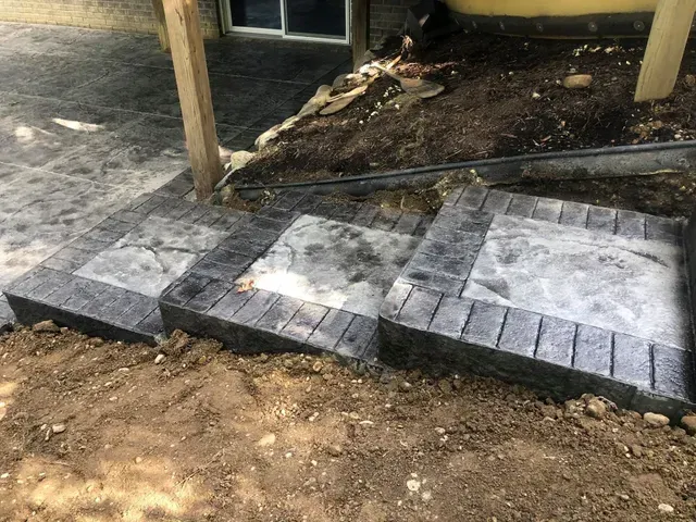 A concrete walkway is being built in the dirt next to a house.