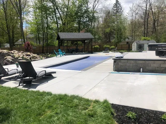 A large swimming pool surrounded by lawn chairs and a gazebo in a backyard.