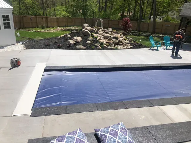 A man is standing next to a swimming pool with a blue cover on it.