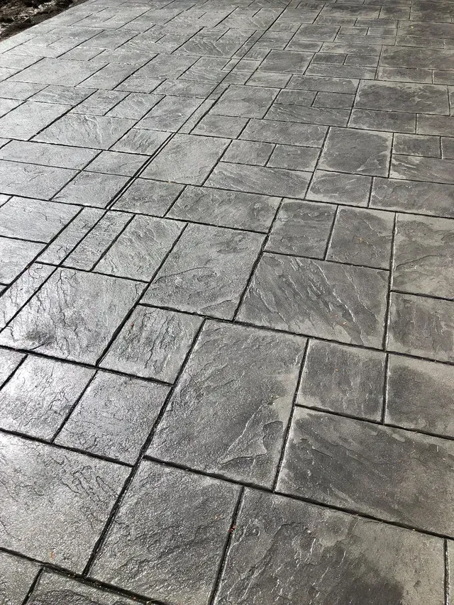 A close up of a concrete driveway with a brick pattern.