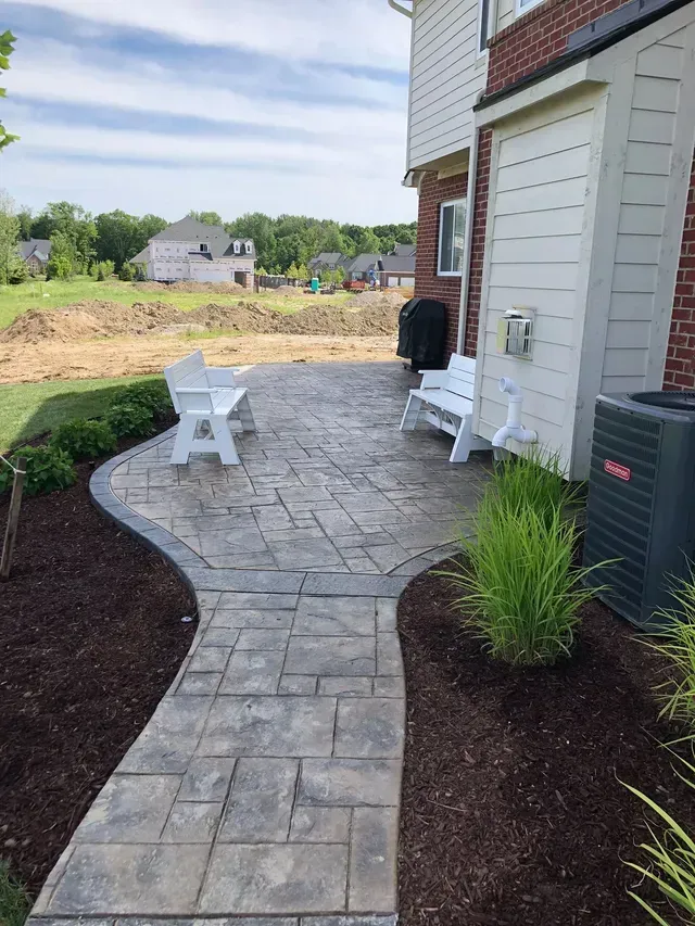 A walkway leading to a patio with chairs and a bench.
