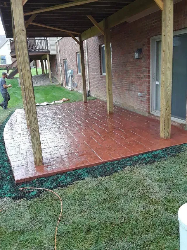 A man is standing under a covered patio in front of a brick house.