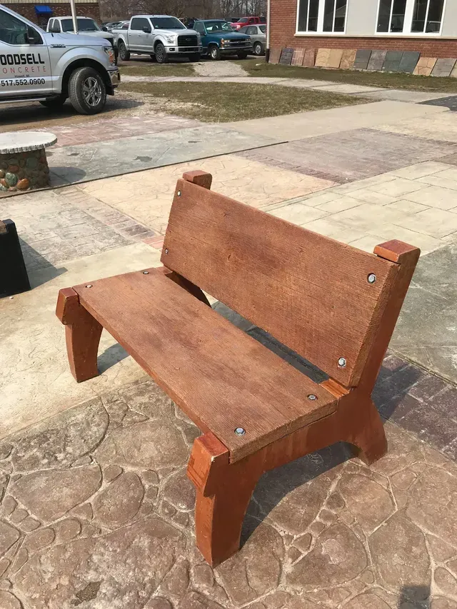 A wooden bench is sitting on a sidewalk next to a parking lot.