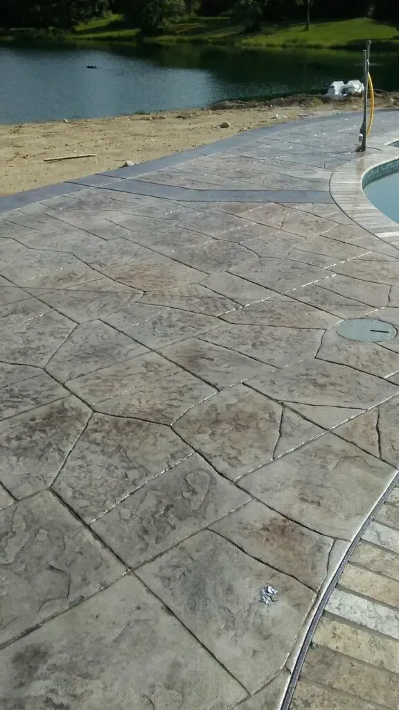 A concrete patio next to a swimming pool with a lake in the background.