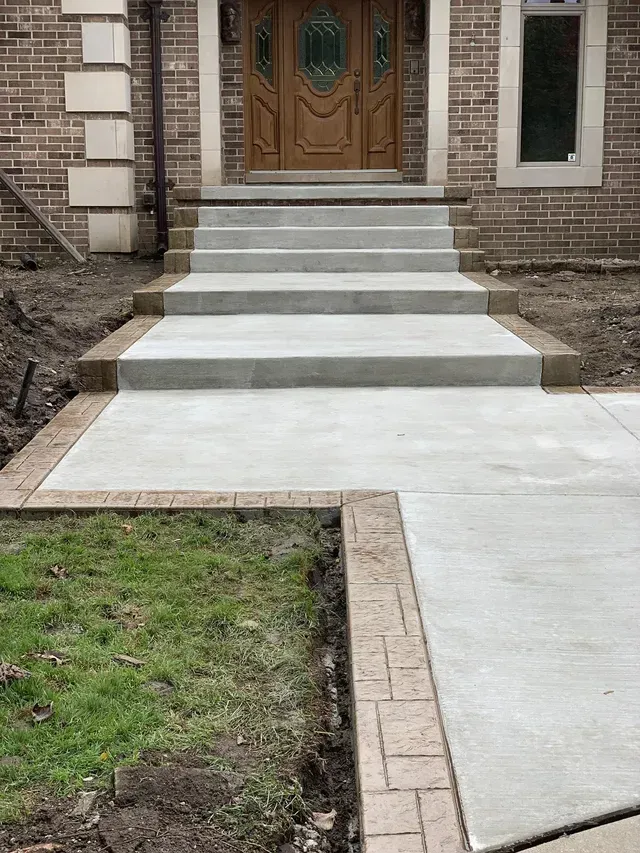 A concrete walkway leading to the front door of a brick house.
