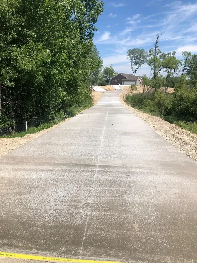 A concrete road with trees on both sides and a house in the background