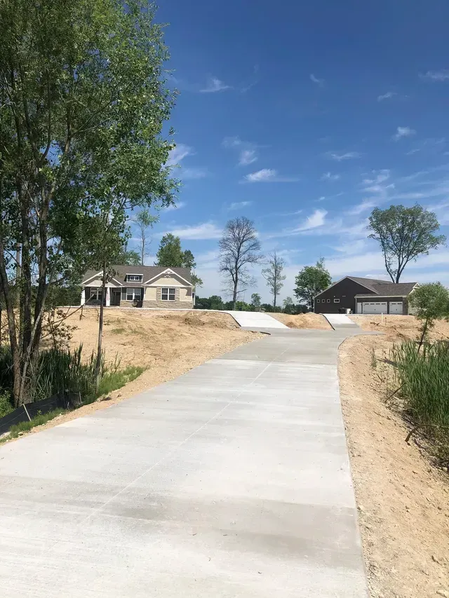 A concrete driveway leading to a house on a hill.
