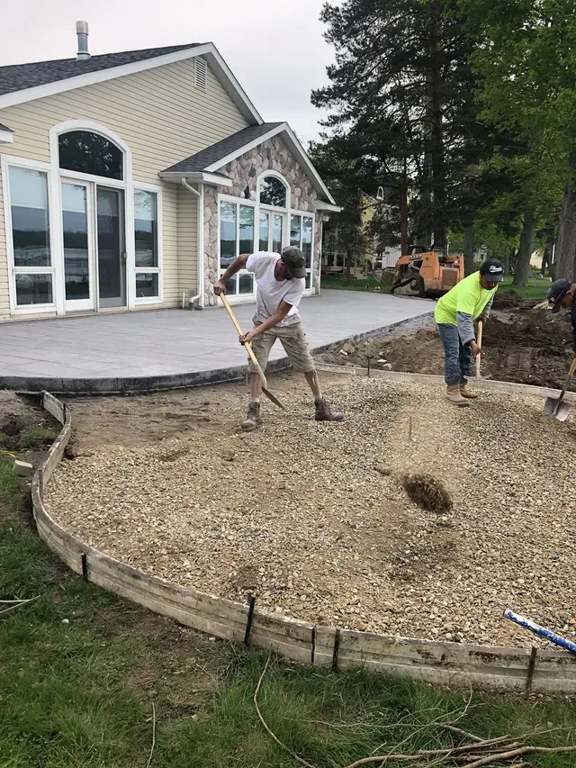 A group of men are working on a concrete patio in front of a house.