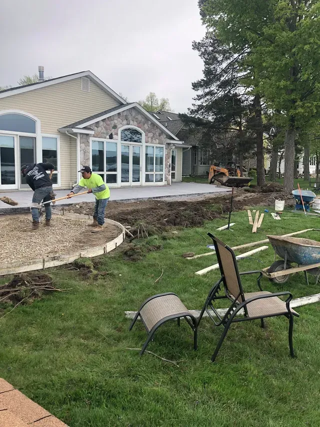 A couple of men are working on a patio in front of a house.
