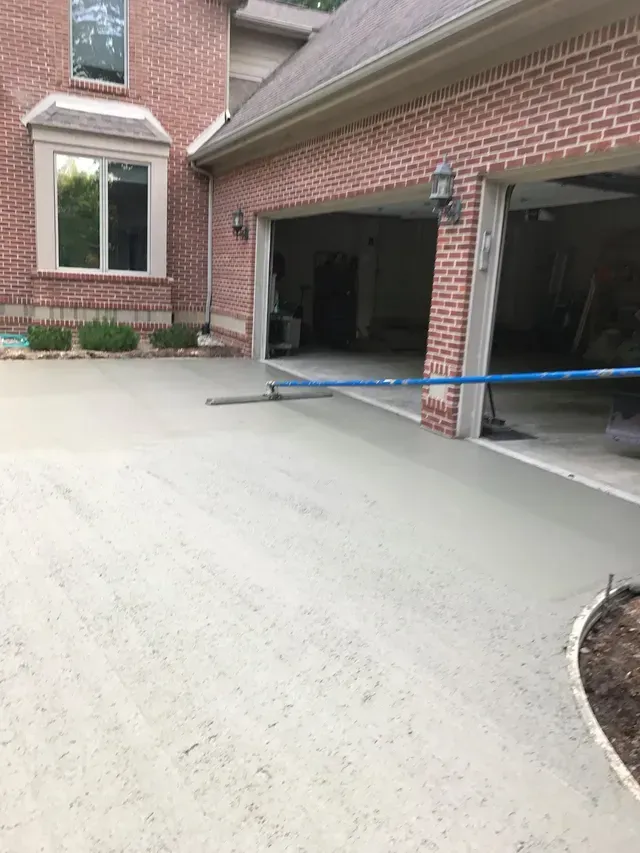 A concrete driveway is being poured in front of a brick house.