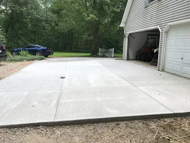 A concrete driveway in front of a garage with a blue car parked in it.