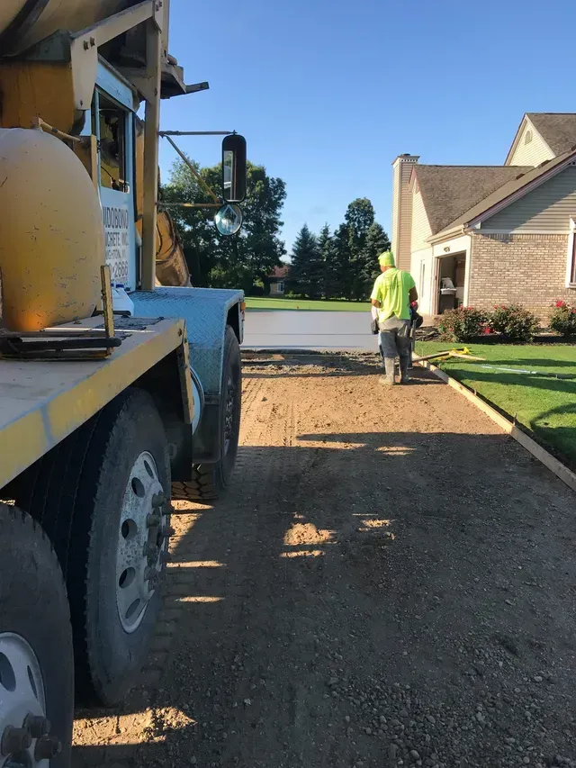 A truck is driving down a dirt road in front of a house.
