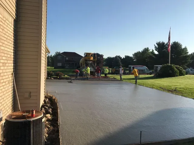 A group of people are working on a concrete driveway in front of a house.