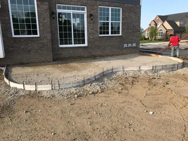 A man is laying concrete in front of a brick house.