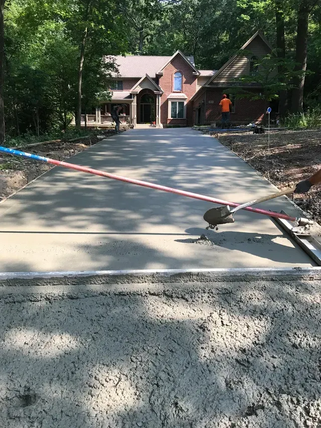 A concrete driveway is being built in front of a large house.