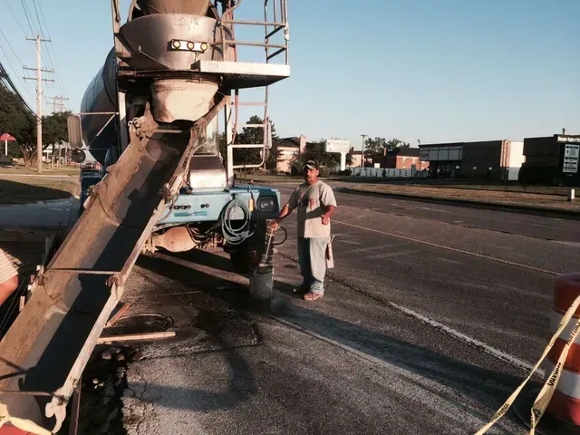 A man is standing next to a concrete mixer on the side of the road