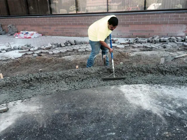 A man is using a rake to spread concrete on the ground